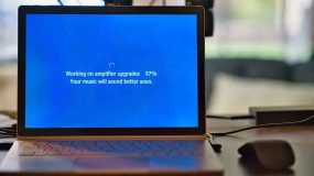 A laptop on a desk with a loading updates message in white on a blue screen